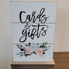 a wooden sign that says cards and gifts with flowers painted on it, sitting on a table