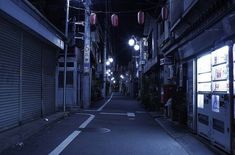 an empty street at night with lights hanging from the building's windows and closed shutters