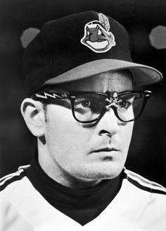 a black and white photo of a baseball player wearing glasses with a hat on his head