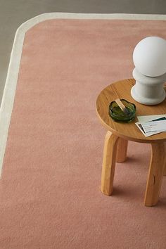 a pink rug with a white vase on it and a small wooden table in the middle