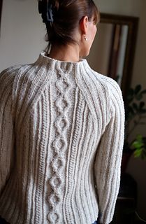 a woman wearing a white sweater and blue jeans standing in front of a mirror with her back turned to the camera