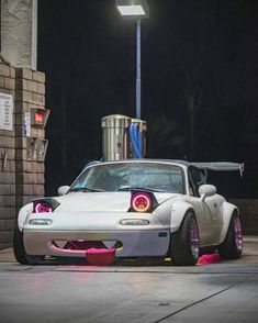 a white sports car parked in front of a brick building at night with its lights on