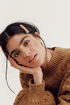 a woman with her chin resting on her hand, wearing a sweater and hair clips