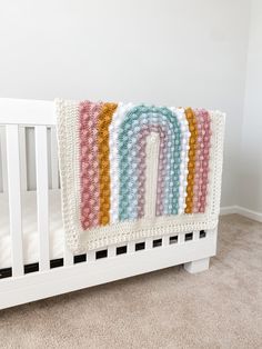 a crocheted rainbow blanket on top of a white crib in a nursery