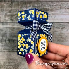 a hand holding a small blue gift box with yellow flowers on it and a bow