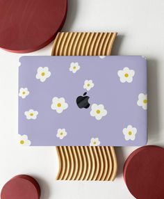 an apple laptop sitting on top of a purple surface with white flowers and circles around it