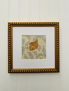 a gold framed artwork hanging on the wall next to a white striped wall with green leaves