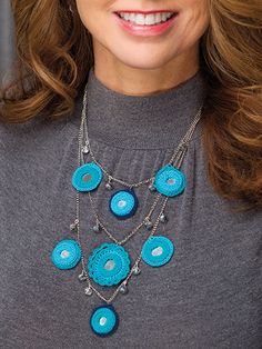 a close up of a woman wearing a necklace with blue buttons and chains on it