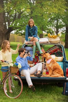 two women and a man are sitting in the back of a truck with their dog