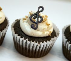 four cupcakes with white frosting and a treble on top are shown