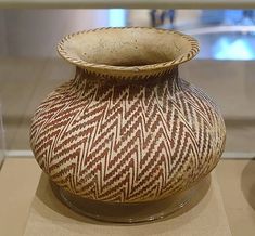 a brown and white vase on display in a glass case