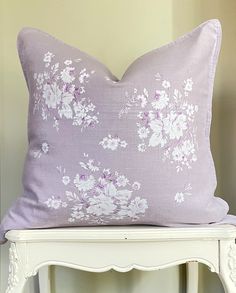 a purple pillow sitting on top of a white chair next to a wooden table and wall