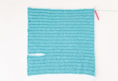 a blue crocheted piece of cloth with a pink thread next to it on a white surface