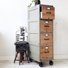 an old metal filing cabinet next to a plant on top of a wooden stool with wheels