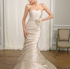 a woman in a strapless wedding dress standing on a wooden floor next to a chair