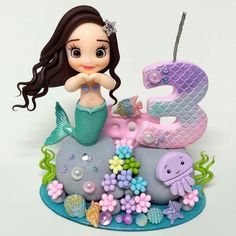 a little mermaid figurine sitting on top of a rock next to a number three