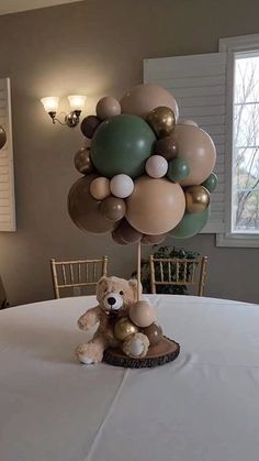 a teddy bear sitting on top of a table with balloons in the shape of a tree