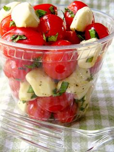 a plastic container filled with lots of fruit on top of a checkered table cloth