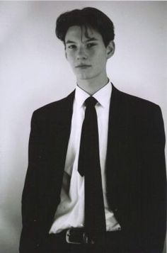 a young man in a suit and tie posing for a black and white photo with his hands on his hips