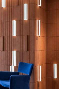 a blue chair sitting in front of a wooden wall with lights on it's sides