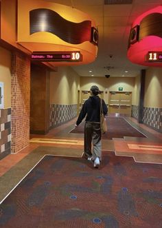 a man walking through a hallway with colorful lights on the ceiling and carpeted floors