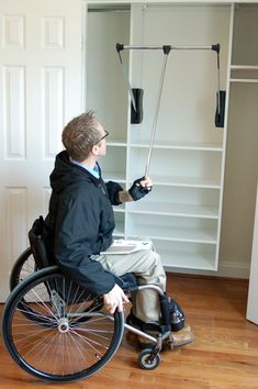 a man sitting in a wheel chair holding an umbrella over his head and looking at the closet behind him