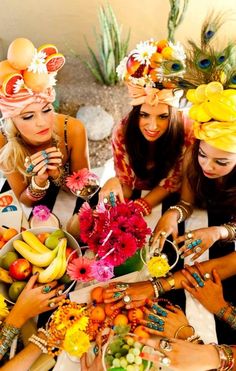 four women wearing headdress around a table with fruit and flowers in their hands