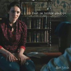 a woman sitting on the floor in front of a bookshelf with a bookcase behind her