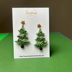 a pair of green christmas tree earrings sitting on top of a card with gold stars