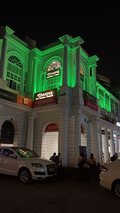 a large building with green lights on it's sides and cars parked in front