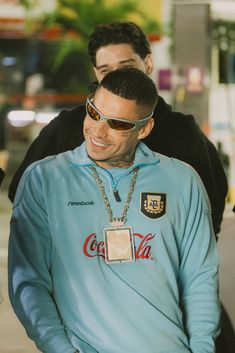 a man wearing sunglasses and a blue sweatshirt with coca cola on it, standing next to another man