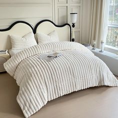 a bed with white comforter and pillows in a bedroom next to a large window