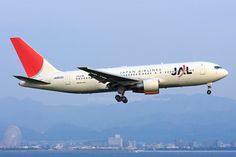 an airplane is flying low over the water and mountains in the background, with one landing gear down