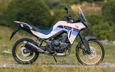 a white and blue motorcycle parked on top of a grass covered field with trees in the background