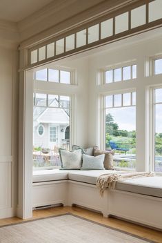 a window seat with pillows on it in front of two large windows and a rug