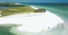 two people are standing on the beach in front of an island with white sand and blue water