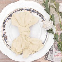 a white plate topped with a piece of cloth on top of a wooden table next to flowers