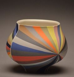 a multicolored striped vase sitting on top of a table next to a gray wall