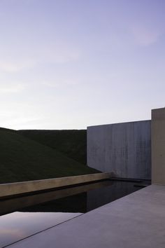 an empty pool in front of a concrete wall and grass covered hill behind it at dusk