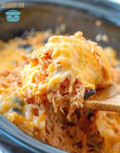 a wooden spoon scooping food out of a casserole dish with cheese and vegetables