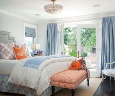 a bedroom with blue curtains and white bedding has an orange bench in front of it