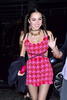 a woman in a pink dress is walking down the street with her hand up to her chest