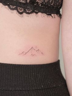 a woman's stomach with a small mountain tattoo on her left side ribcage