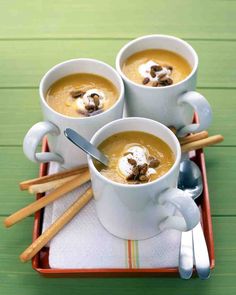 three white mugs filled with soup on top of a wooden tray next to utensils