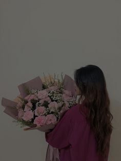 a woman holding a bouquet of pink roses in her hand and looking at the wall