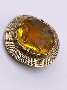 "Vintage Accessocraft NYC pin brooch. Gold tone with a large, yellow topaz colored faceted glass stone. Setting features a delicate rope texture. The glass gem is topaz yellow color with a wide streak of darker  amber orange color in center. Surface of glass gem is free of scratches. Brooch is marked \"ACCESSOCRAFT N.Y.C.\" A unique, show stopping statement piece!" Antique Gold Brooch With Gemstone, Antique Gold Gemstone Brooch, Yellow Brooch For Formal Occasions, Gold Gemstone Round Brooch, Gold Gemstone Round Brooches, Round Gold Brooches With Gemstone, Round Gold Brooch With Gemstone, Gold Jeweled Costume Jewelry Brooches, Gold Costume Jewelry Brooches With Jewels