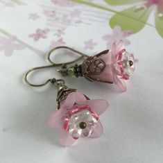 "Pretty in Pink... Add some spring to your wardrobe with these lovely double pink blossoms. Delicate pink petals surround bright pink and white centers. Antique brass filigree caps adorn the tops and a tiny green bead adds a bit of spring pop. These earrings are very lightweight and comfortable to wear. Perfect for a garden wedding, or a gift for a nature lover. And don't forget...Mother's Day is just around the corner. Drop length from bottom of antique brass french earwire: 1\" (25mm) Prefer a Handmade Feminine Flower-shaped Earrings, Handmade Feminine Flower Earrings, Handmade Feminine Flower Shaped Earrings, Handmade Flower Earrings As Feminine Gift, Feminine Handmade Flower Earrings For Gift, Handmade Feminine Flower Earrings For Gifts, Rose Red Flower Earrings, Pink Flower Decoration Drop Earrings, Pink Petal-shaped Jewelry For Spring