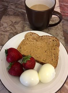 a white plate topped with toast, eggs and strawberries next to a cup of coffee