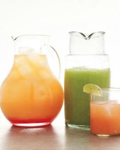 three pitchers and two glasses filled with different types of juices on a counter top