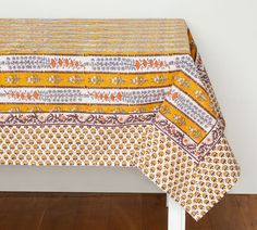 a yellow and white table cloth with an intricate design on it, sitting on a wooden floor